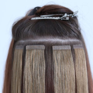 Several tape-in hair extensions are being attached to natural hair, which is sectioned and clipped up with metal hair clips—essential for those caring for hair extensions. - Mermaid Hair Extensions in Kirkland and Seattle, WA